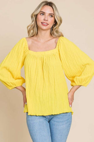 Woman wearing yellow square neck puff sleeve top with a flattering fit and ruched details, paired with jeans.