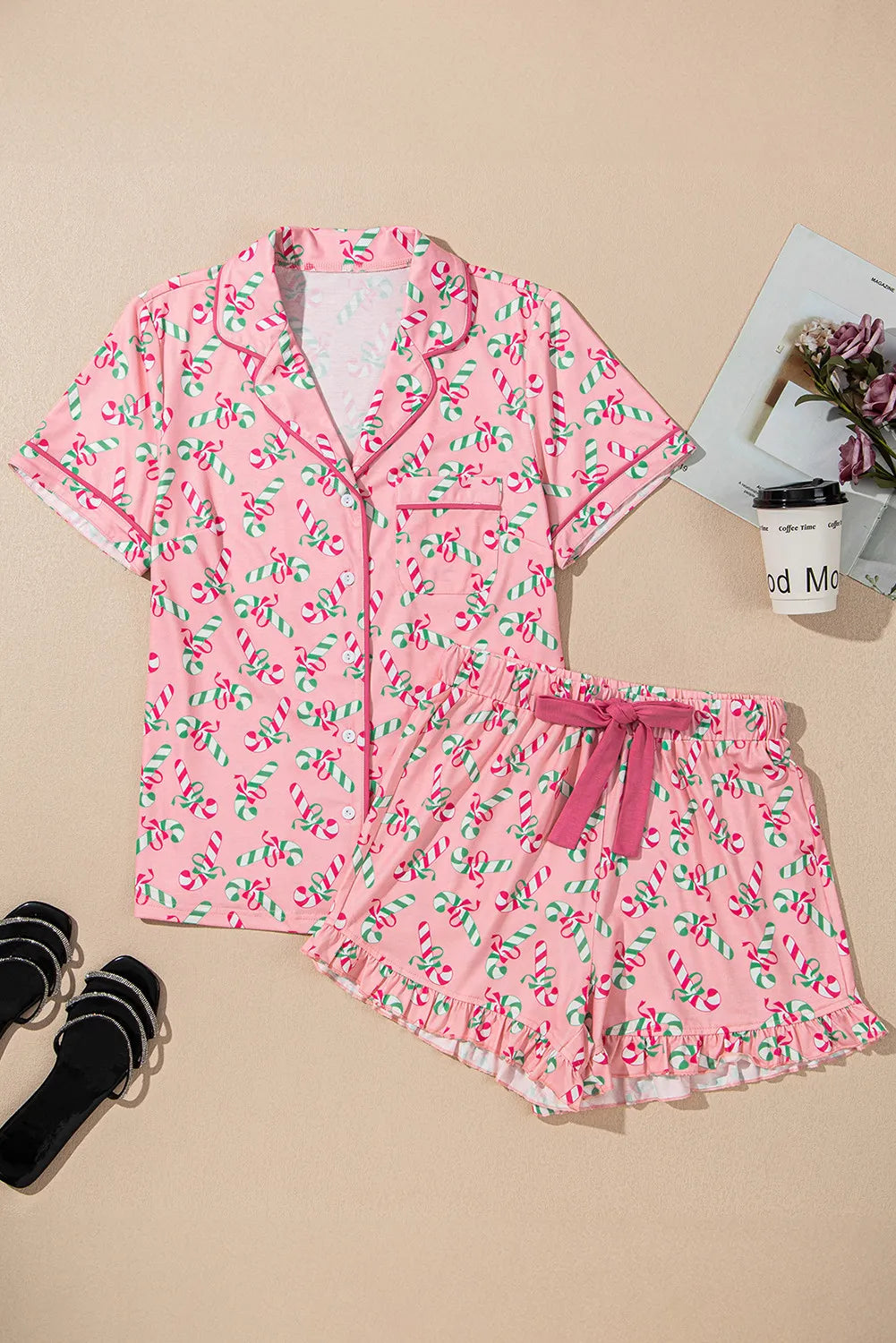 Pink candy cane printed collared neck top and shorts pajama set with black slippers and magazine backdrop.