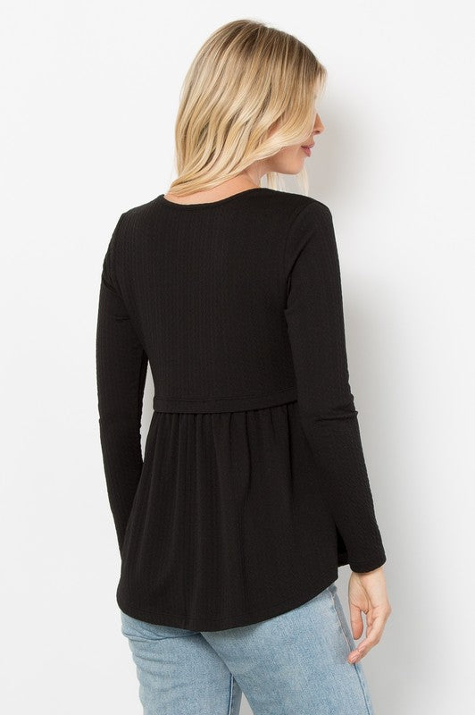 Woman wearing black round neck long sleeve knit top with peplum detail and cable-knit texture, styled with blue jeans.