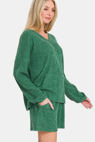 Woman wearing dark green V-neck ribbed top and shorts set, long sleeves, two-piece, slightly stretchy material.