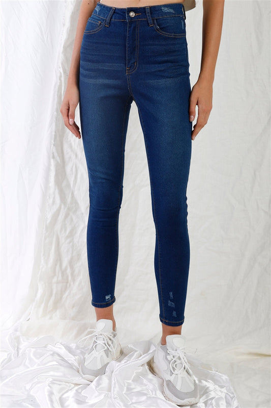 Dark blue high-waisted skinny jeans with small rips, contrast stitching, and five-pocket design, paired with white sneakers.