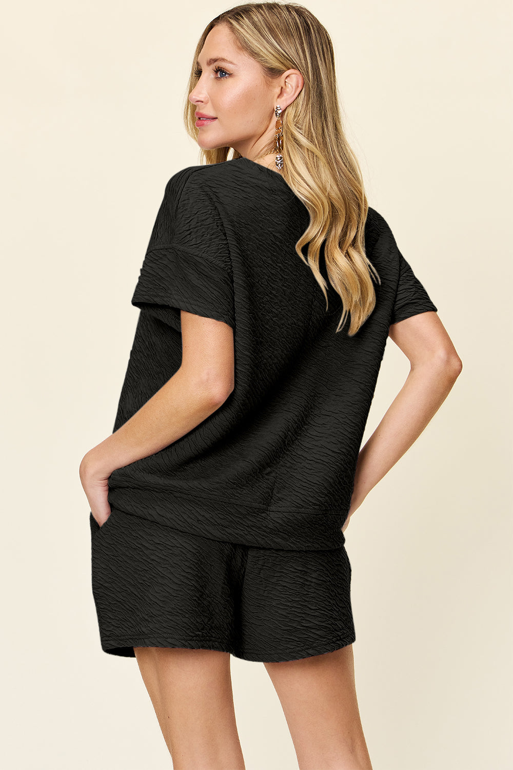 Woman wearing a black textured short sleeve t-shirt and drawstring shorts set with pockets, made of stretchy polyester-spandex blend.