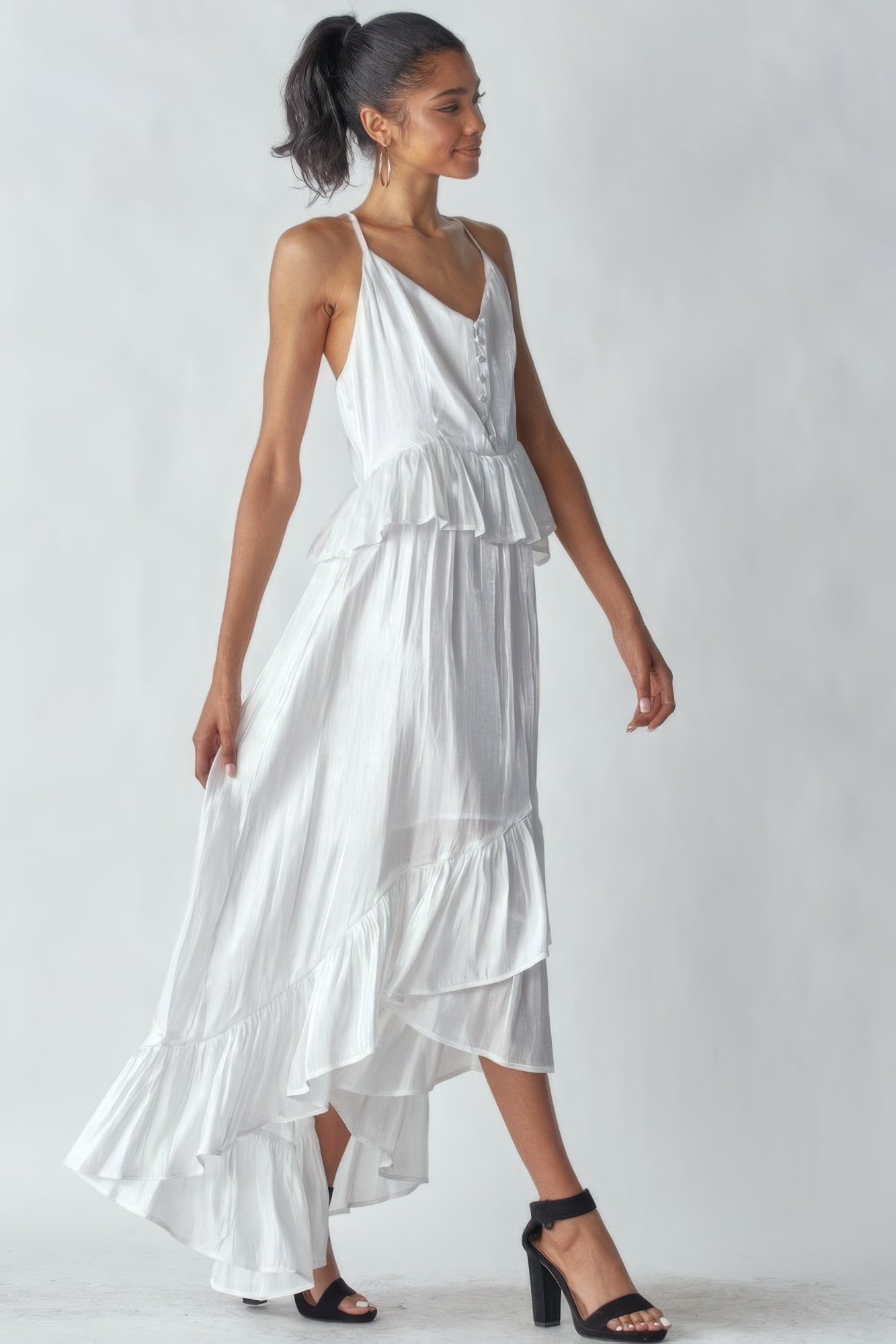 Woman wearing a sleeveless, shimmering white dress with ruffles and asymmetric hemline, perfect for special occasions.