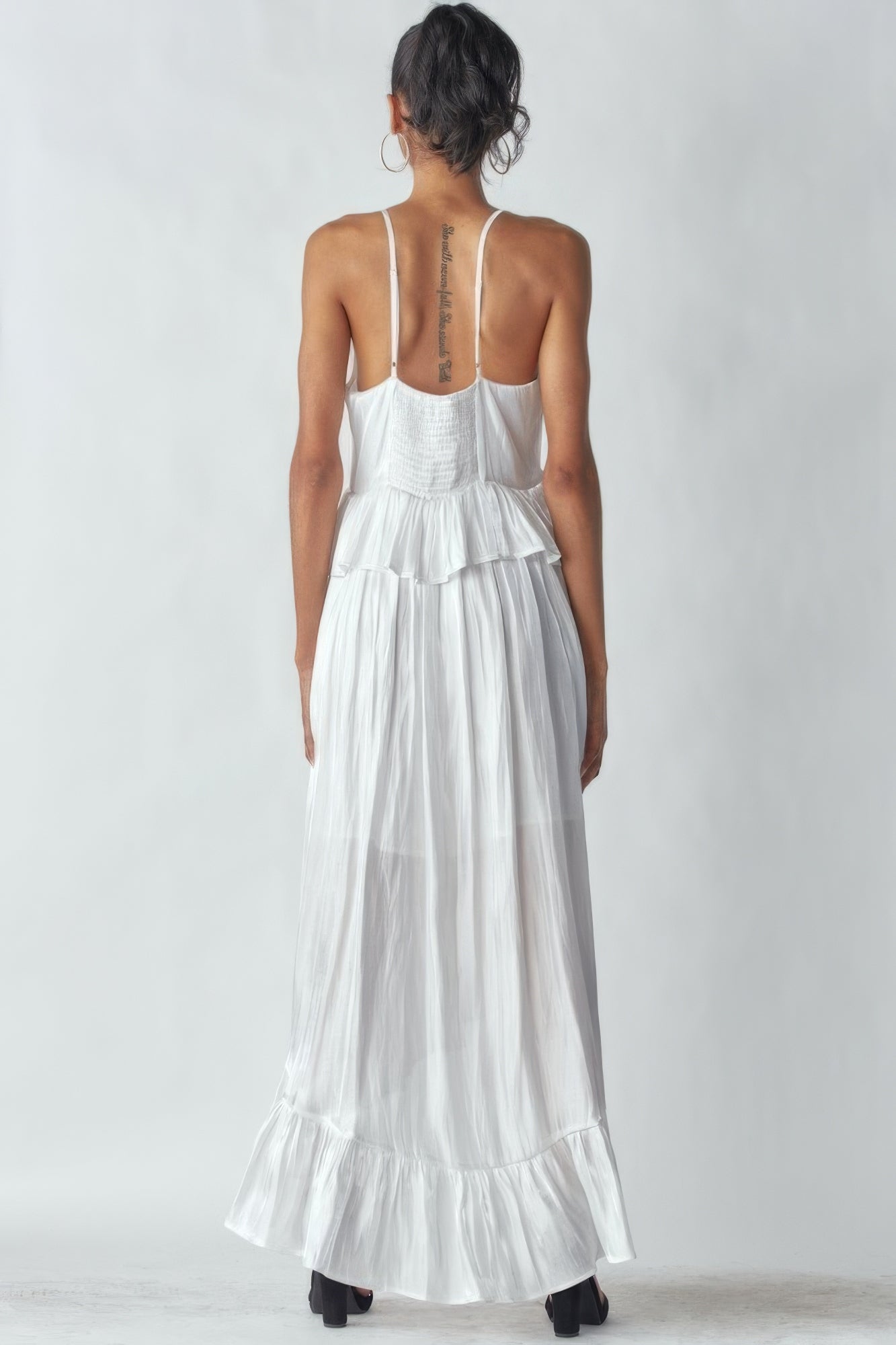 Woman wearing white shimmering sleeveless dress with ruffles and adjustable straps, showcasing the elegant asymmetric design.