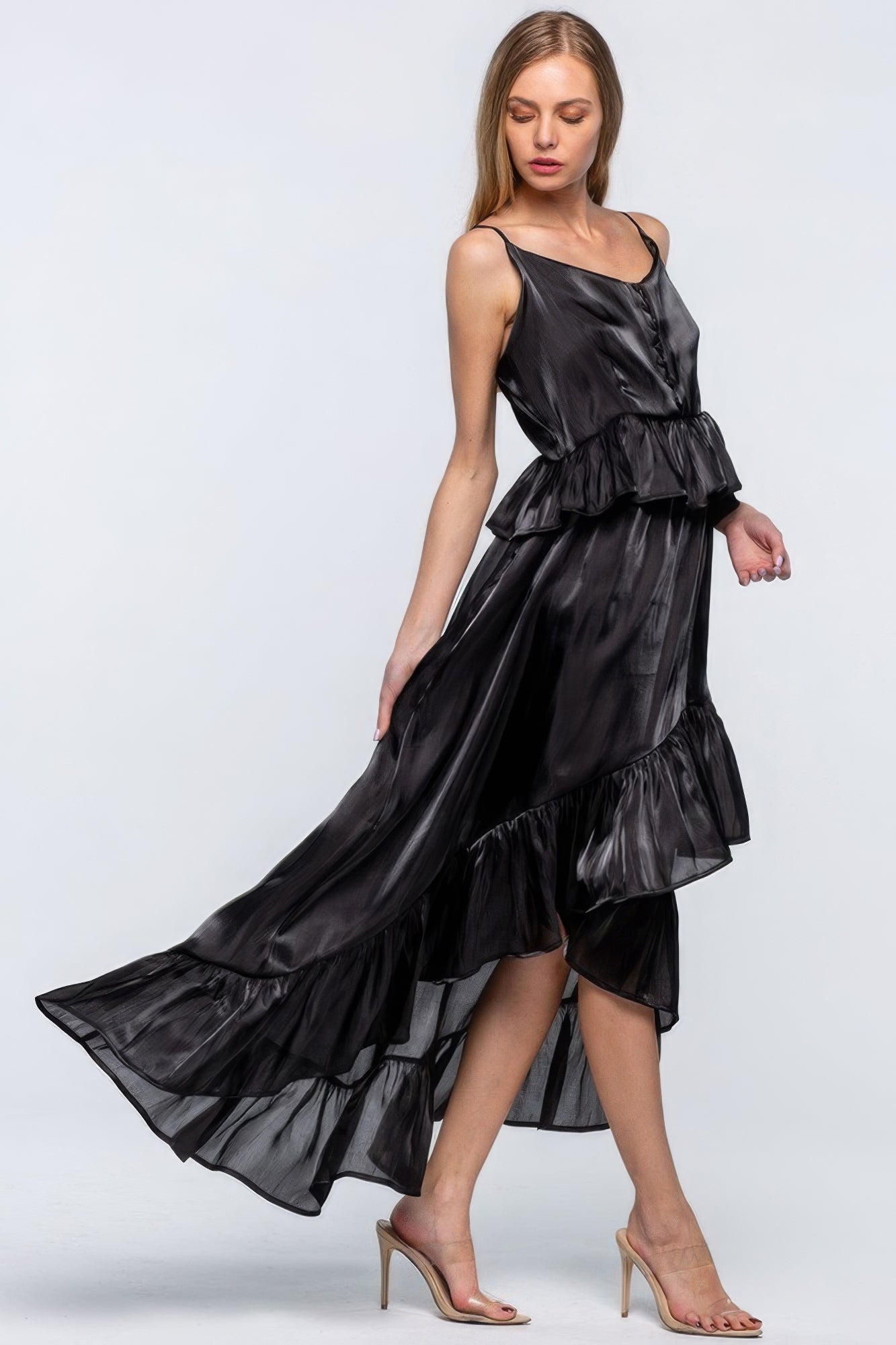 Woman wearing a shimmering sleeveless dress with ruffles, featuring an asymmetric hemline and adjustable straps, in chic black color.