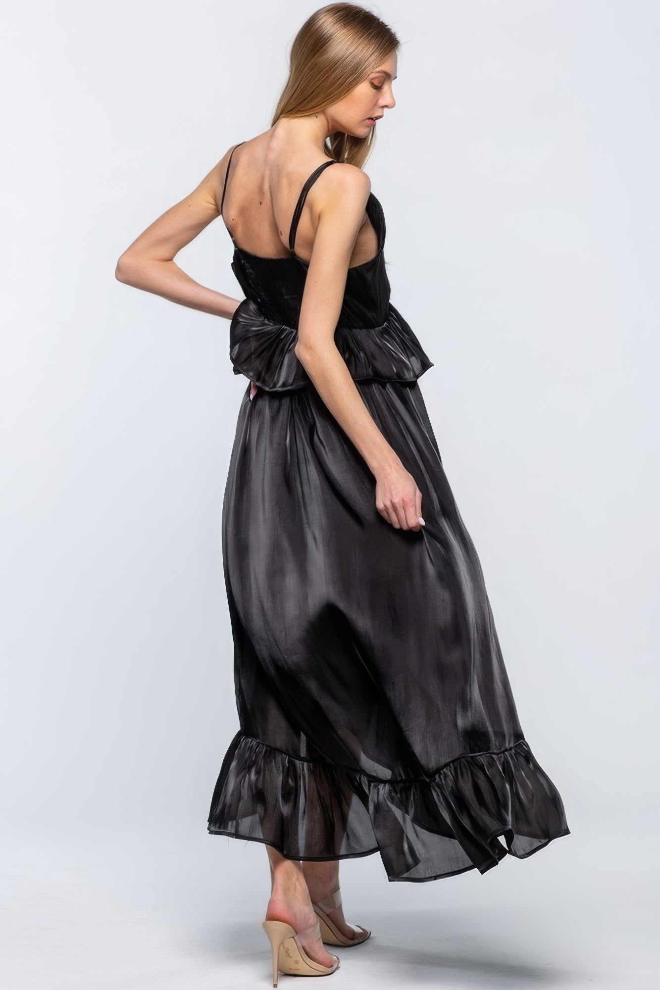 Woman wearing a sleeveless shimmering dress with ruffles, adjustable shoulder straps, and an asymmetric hemline in chic black.