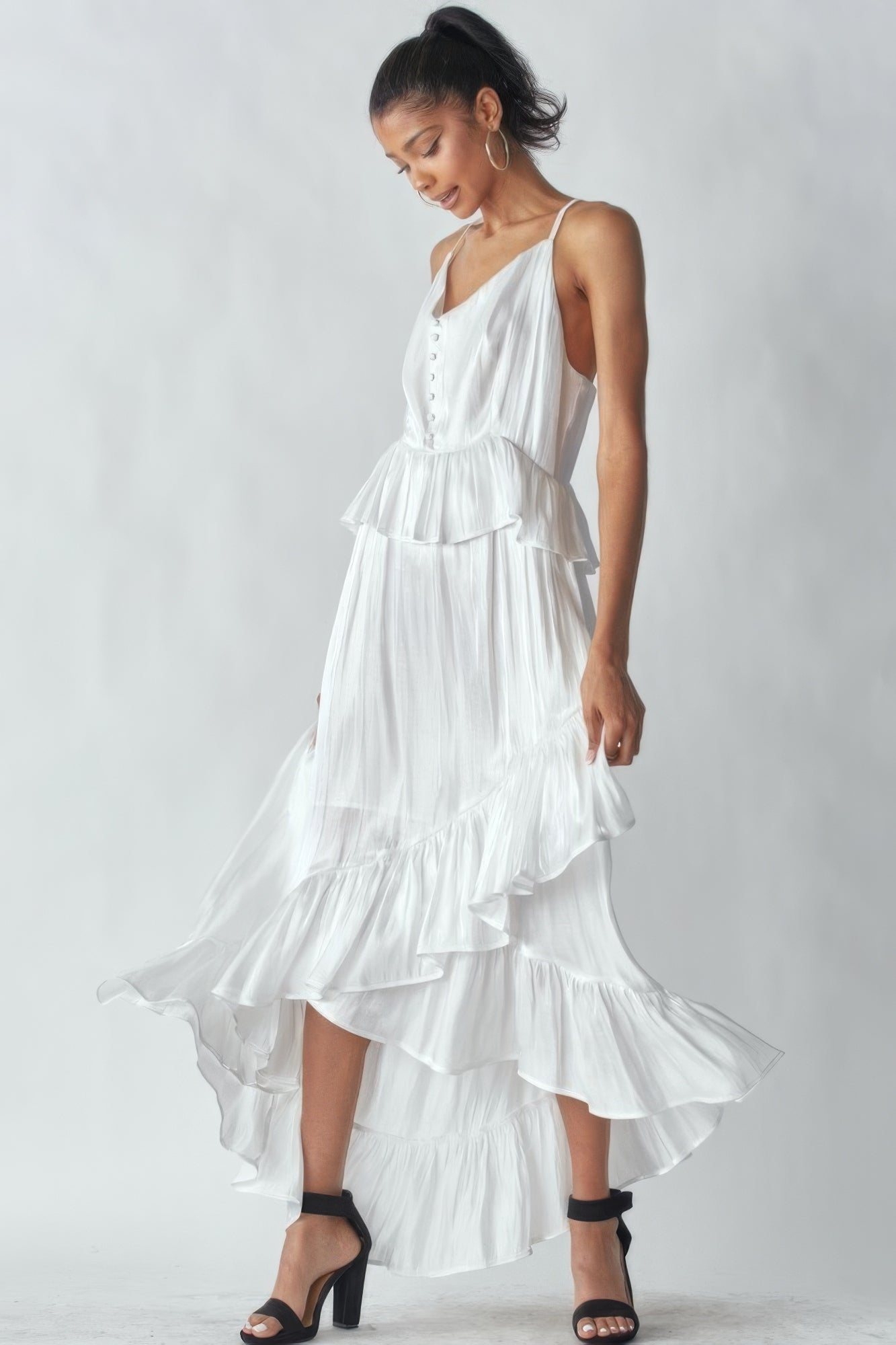 Woman wearing sleeveless white shimmering dress with ruffles and asymmetric hemline, highlighting elegant style and adjustable straps.