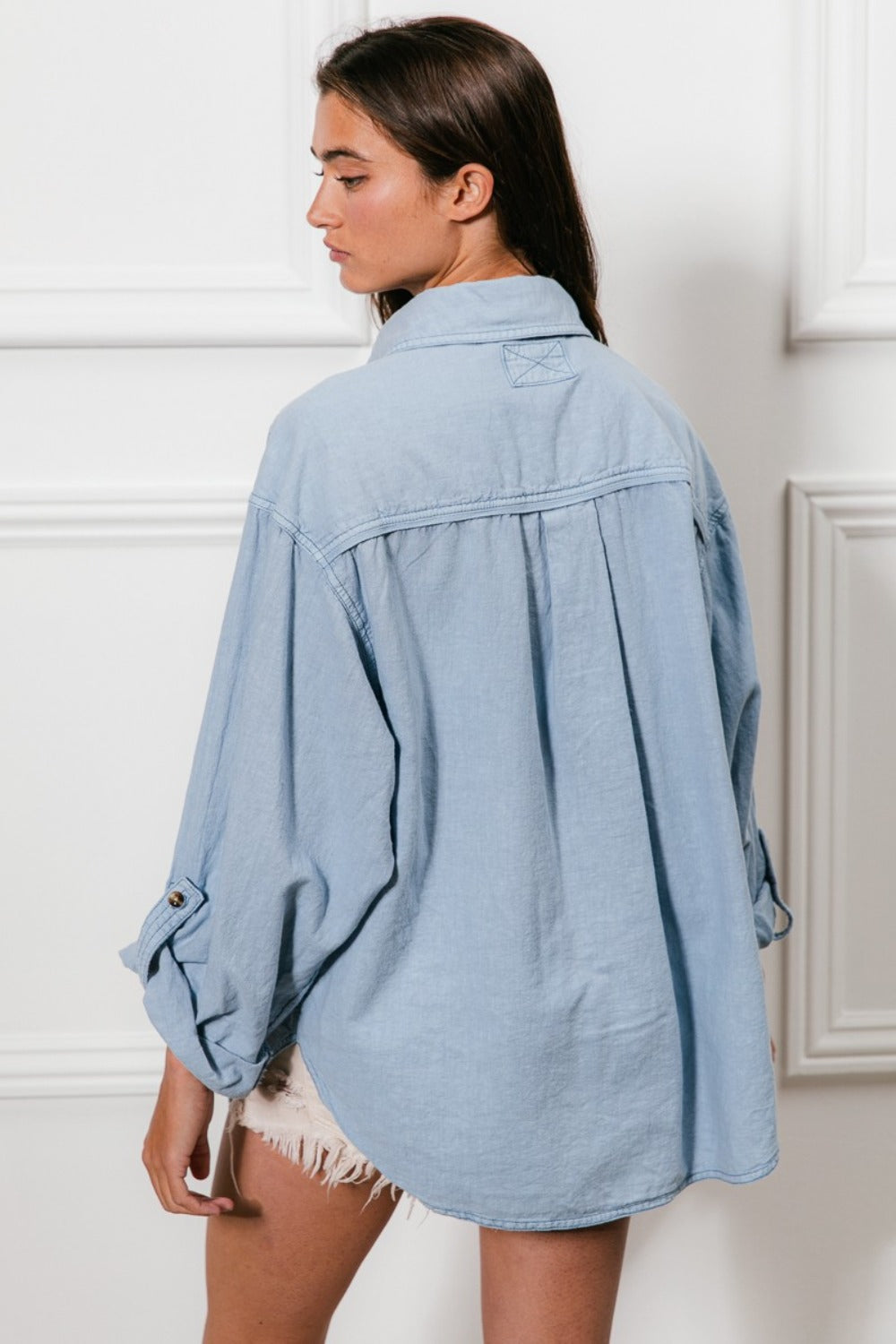 Woman wearing a denim button-down shirt with stitch detail and chest pockets, showcasing back view and relaxed fit.