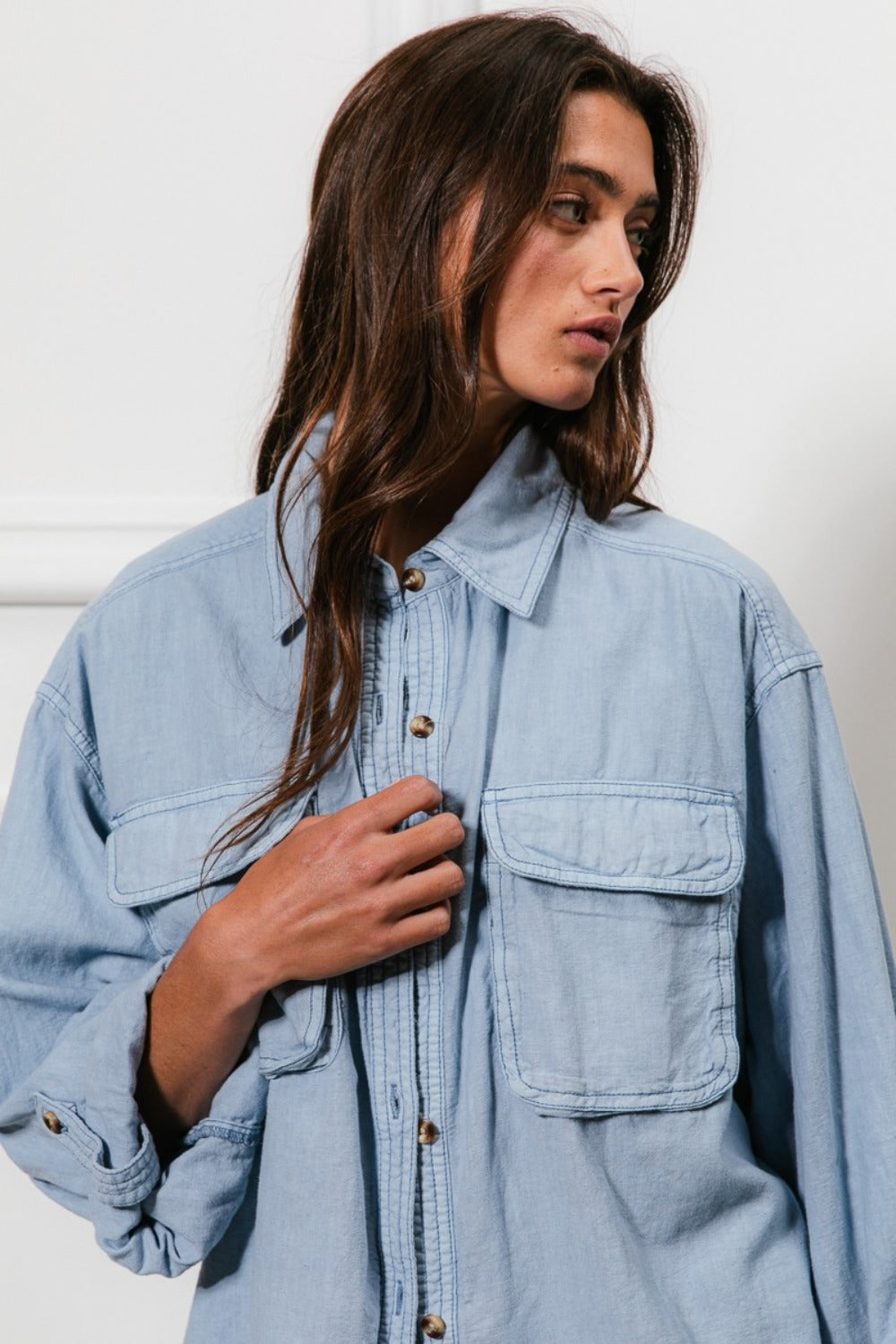 Woman wearing a denim button down shirt with chest pockets and stitch detail.