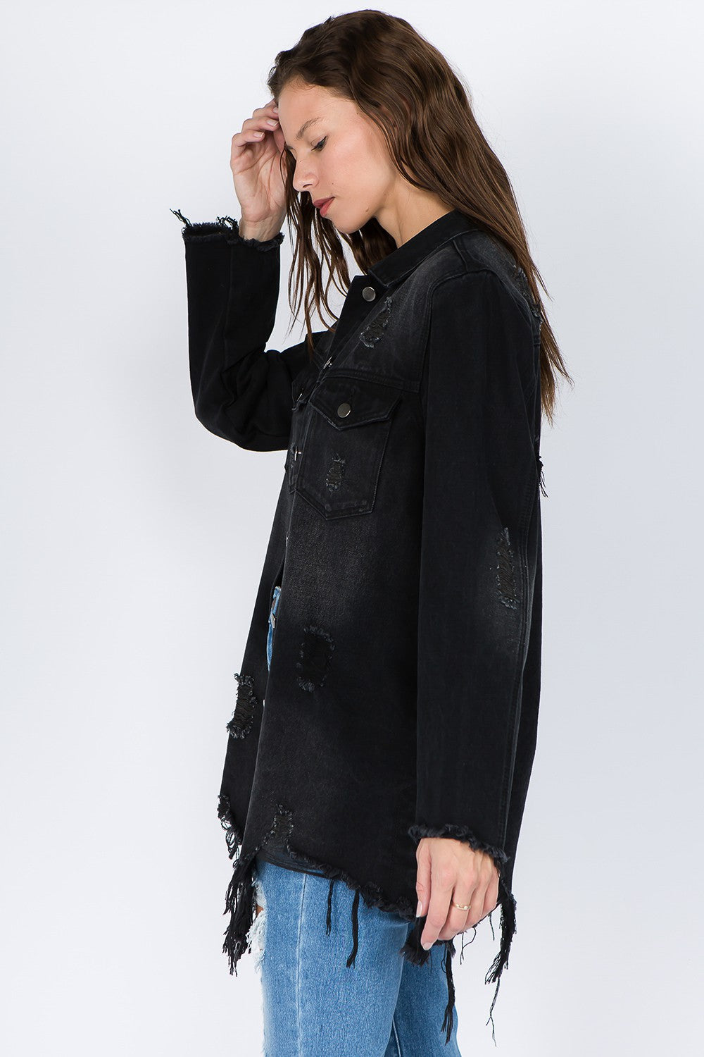 Woman wearing a distressed frayed hem denim jacket with a raw hem and button-front closure, perfect for versatile layering.