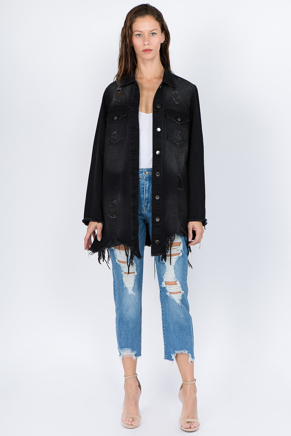 Woman wearing distressed frayed hem denim jacket with button-front closure, paired with ripped jeans and heels. Trendy fashion.