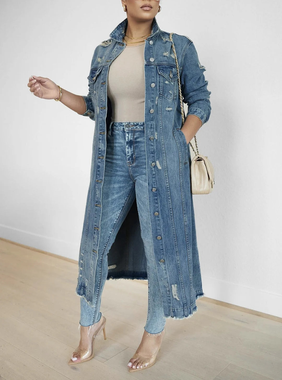 Distressed denim long jacket with frayed hem, oversized fit, and versatile wash, styled over jeans and a beige top in a modern look.