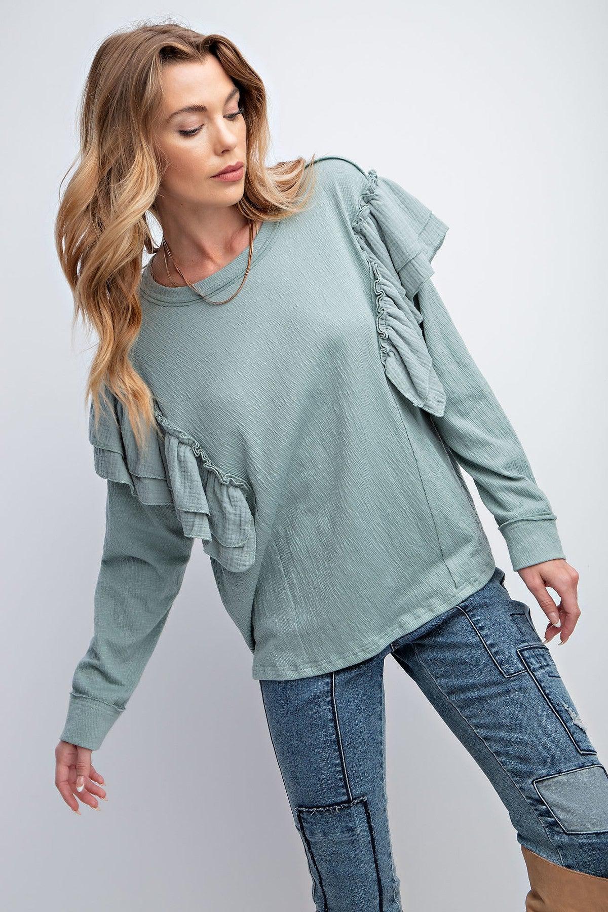 Woman wearing a faded blue top with double ruffle sleeves, rounded neckline, loose fit, and dropped shoulders.