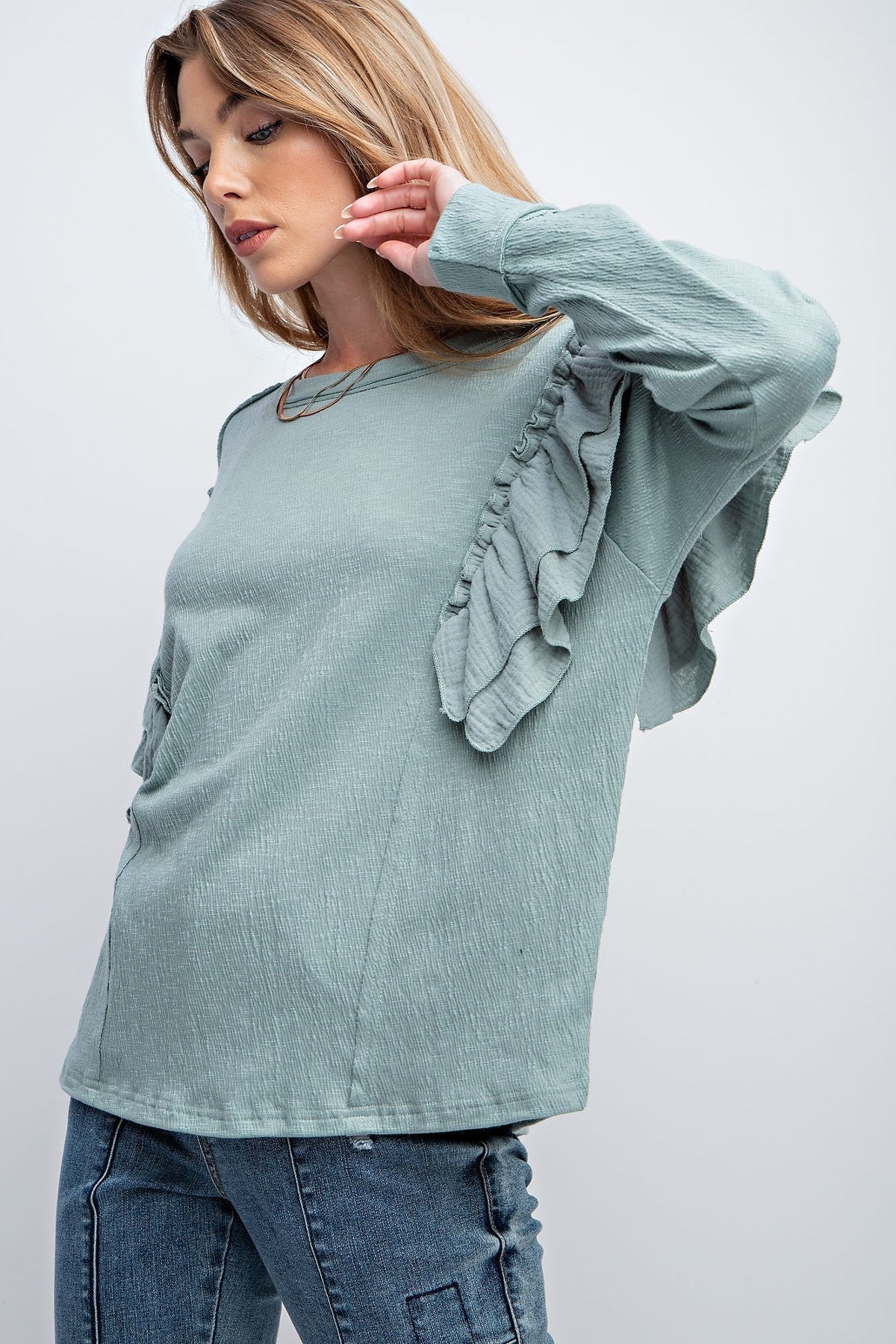 Woman wearing faded blue top with double ruffle sleeves, rounded neckline, loose fit, and dropped shoulders.