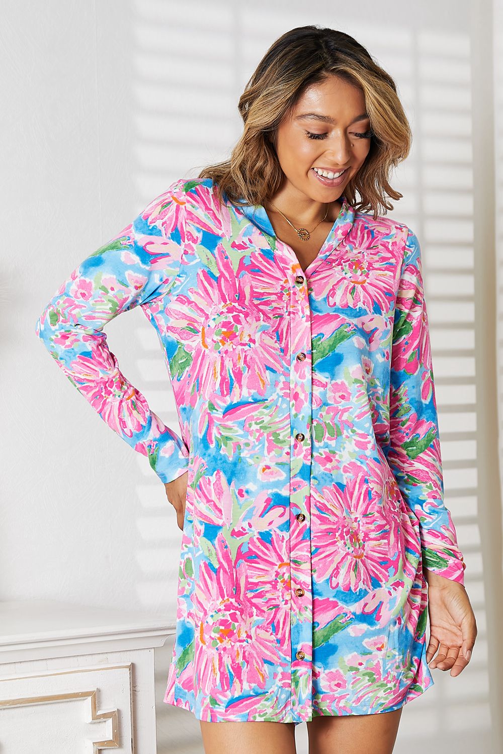 Woman wearing a floral open front long sleeve cardigan with colorful pink and blue flower design, standing in a bright room.