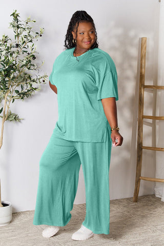 Woman wearing a trendy mint green round neck slit top and pants set in soft rayon blend, standing indoors near a plant.