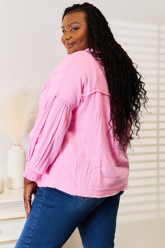 Woman wearing pink exposed seam blouse with buttoned notched neck, paired with jeans for a casual yet polished look.