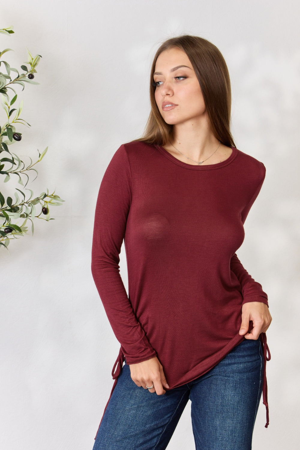 Woman wearing a drawstring round neck long sleeve top in burgundy, made of stretchy rayon and spandex blend, paired with jeans.