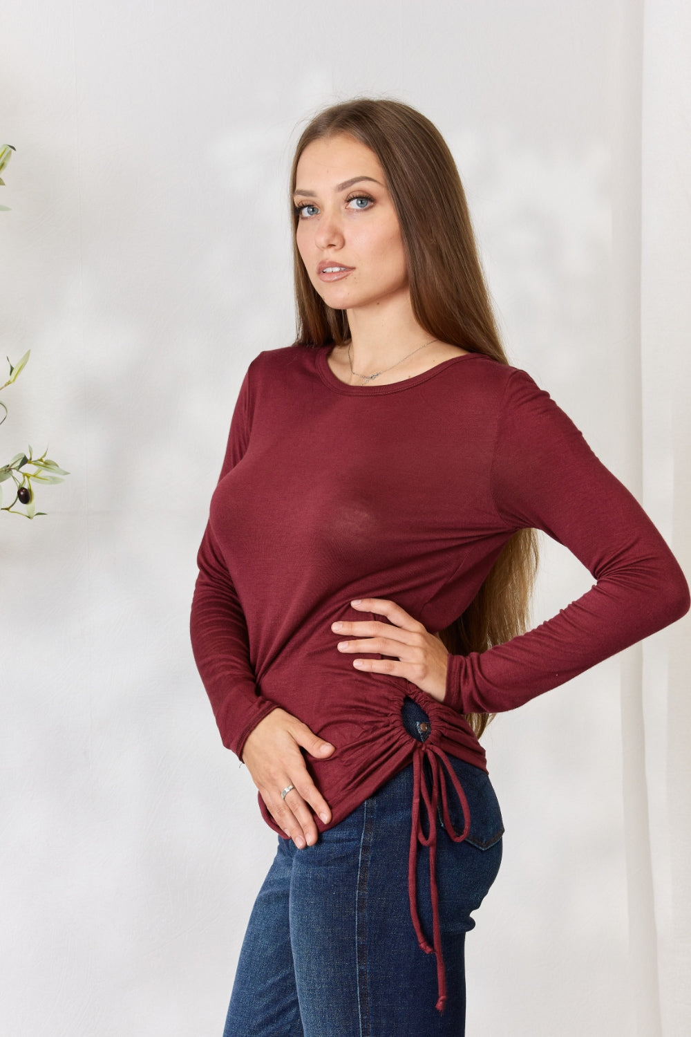 Woman wearing burgundy drawstring round neck long sleeve top with a fitted design, styled with jeans.