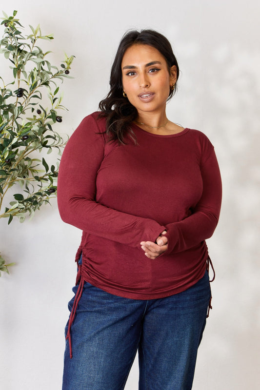 Woman wearing drawstring round neck long sleeve top in burgundy, made of stretchy rayon and spandex, paired with jeans.