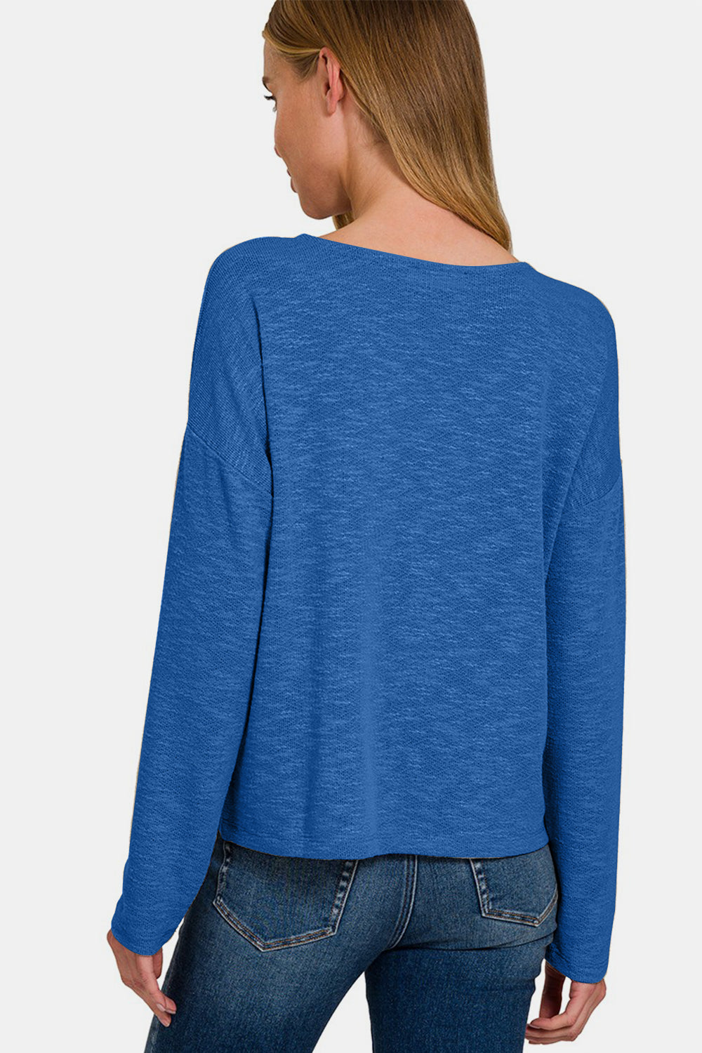 Woman wearing blue dropped shoulder long sleeve t-shirt, showcasing back view and relaxed fit, paired with jeans.