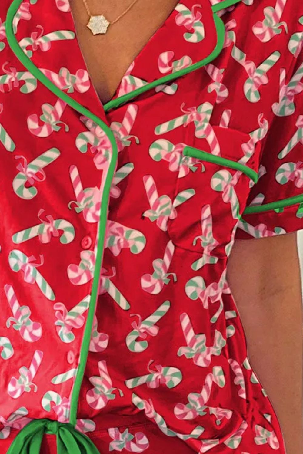 Woman wearing red candy cane print collared neck top, part of pajama set with green trim, featuring festive holiday design.