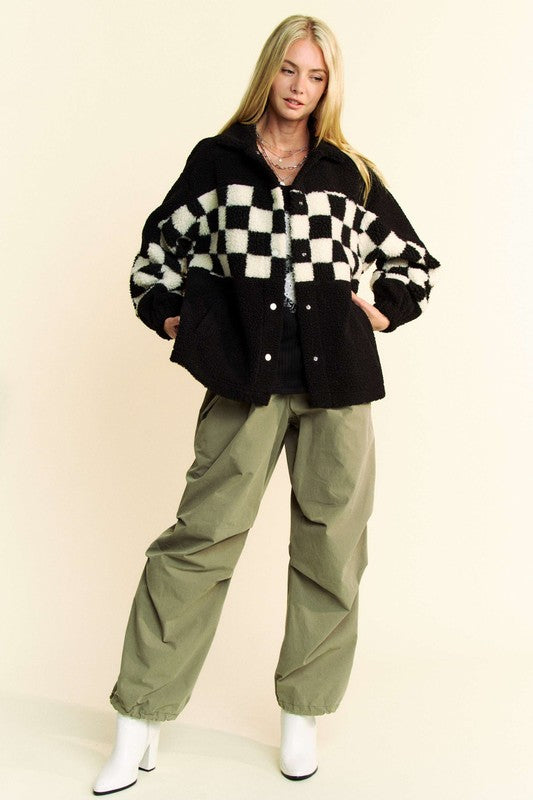 Woman wearing black checkered faux fur jacket with pockets and green pants.