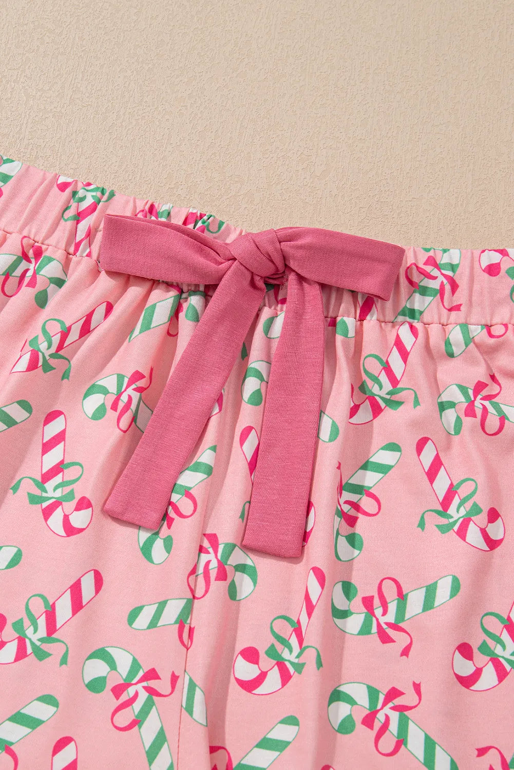 Pink pajama shorts with candy cane pattern and drawstring bow detail, part of a two-piece set, slightly stretchy polyester-elastane fabric.