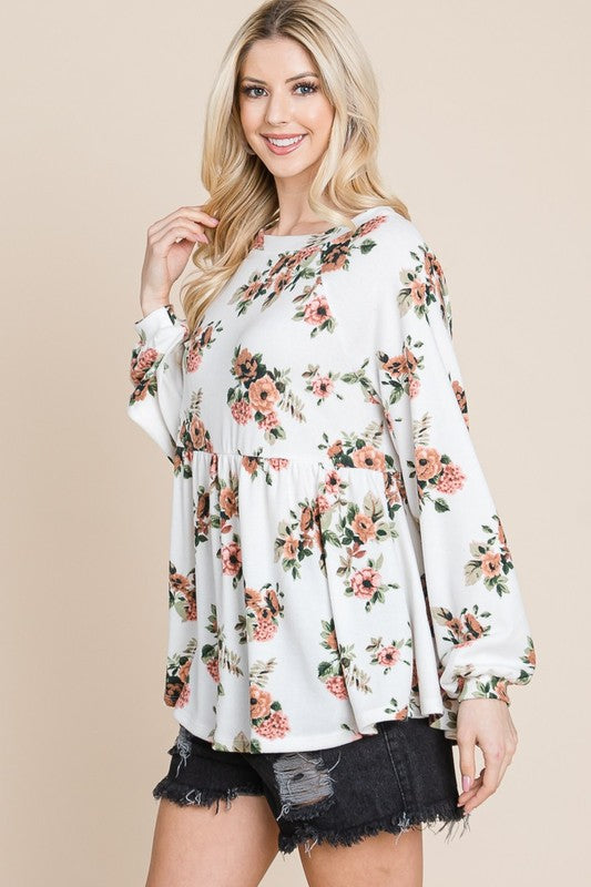 Woman wearing floral full-size babydoll blouse with boat neck and long sleeves, paired with black shorts.