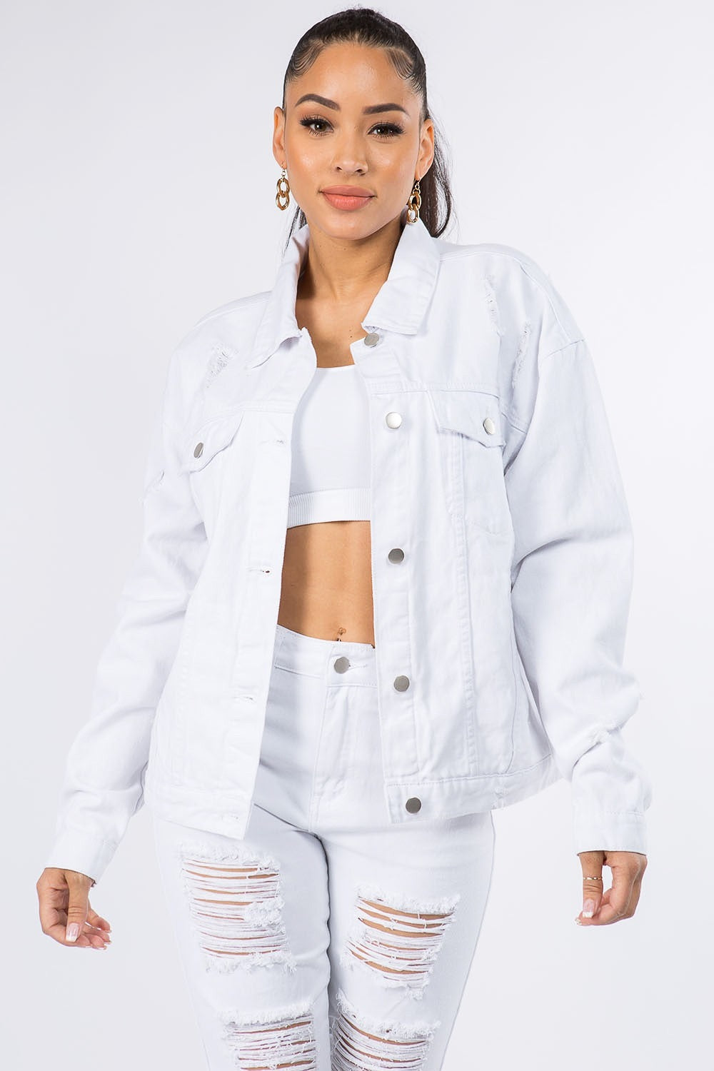 Woman wearing a graphic distressed long sleeve denim jacket, paired with a white crop top and ripped jeans for an edgy look.