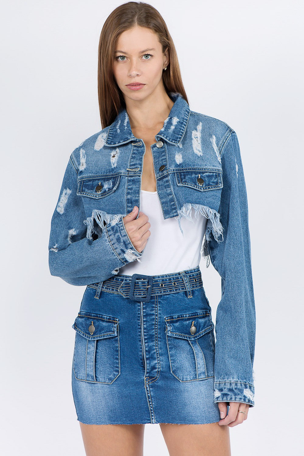 Woman wearing distressed denim jacket with frayed hem, paired with denim skirt, showcasing edgy and trendy fashion outfit.