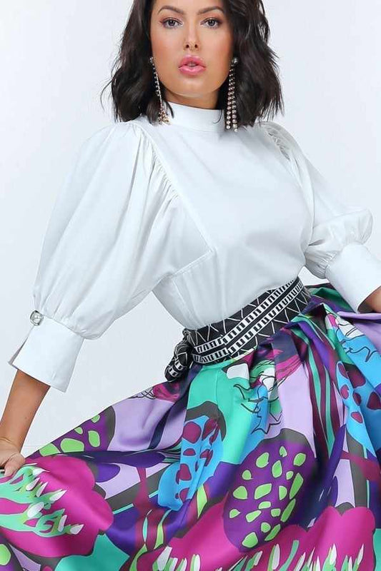 Woman wearing off-white puff sleeve blouse with pearl buttons and a colorful floral skirt.