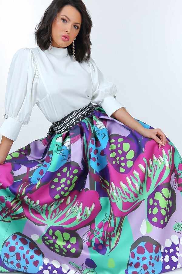 Woman wearing off-white puff sleeve blouse with pearl buttons and vibrant floral skirt.