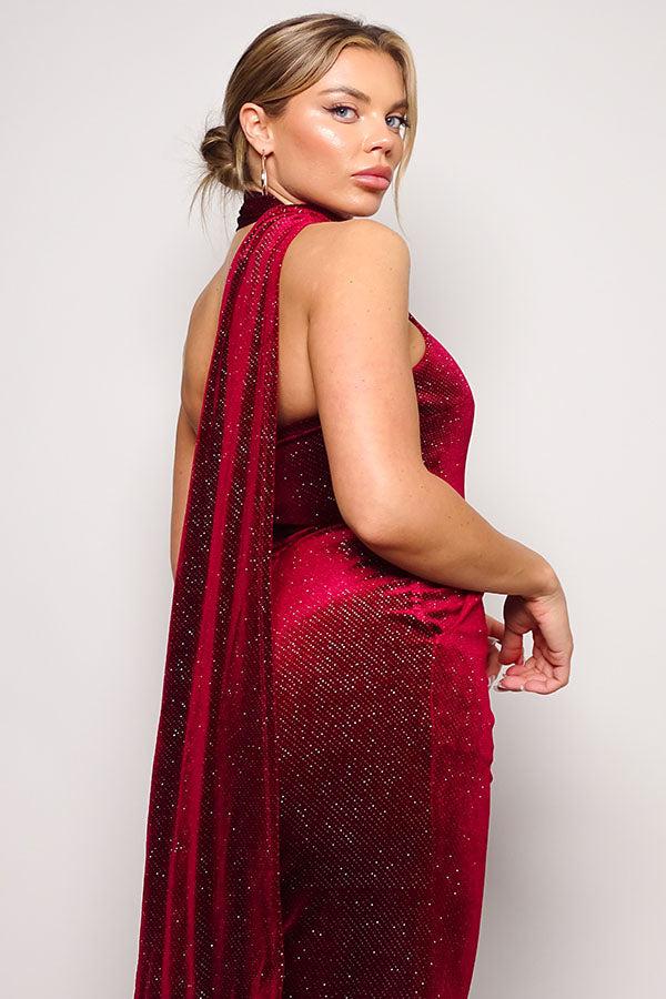 Red glitter velvet jumpsuit with scarf detail, one-shoulder, and open back. Model showcases elegant evening wear.