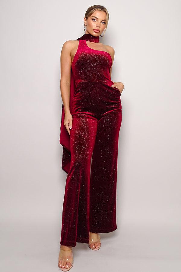 Red glitter velvet jumpsuit with one-shoulder sleeveless design, wrap-around scarf, and open back, featuring long pants and side pockets.