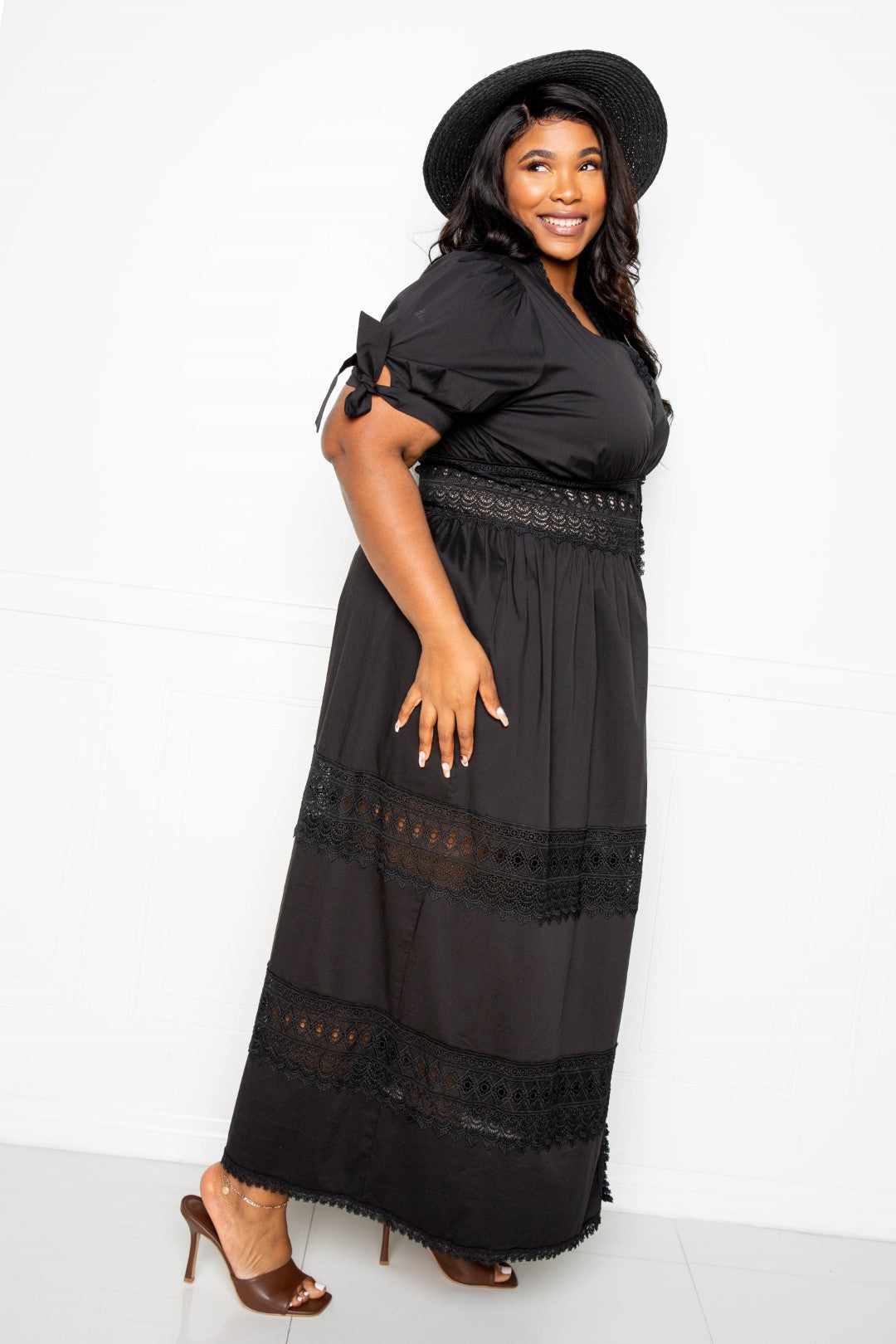 Woman wearing a black puff sleeve maxi dress with lace insert and a black hat.