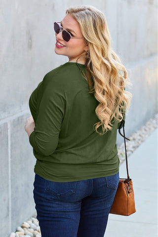 Woman wearing a green round neck batwing sleeve top with sunglasses, styled with jeans and a brown handbag, casual fashion look.