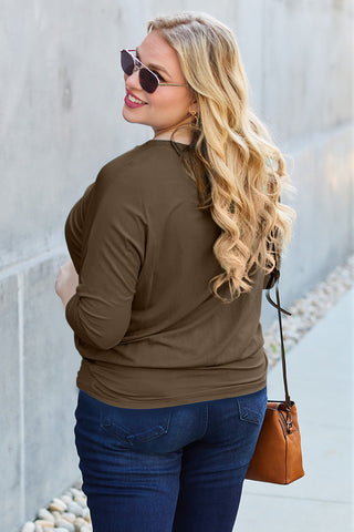 Woman wearing round neck batwing sleeve top in brown, paired with jeans and sunglasses, standing outside with a handbag.