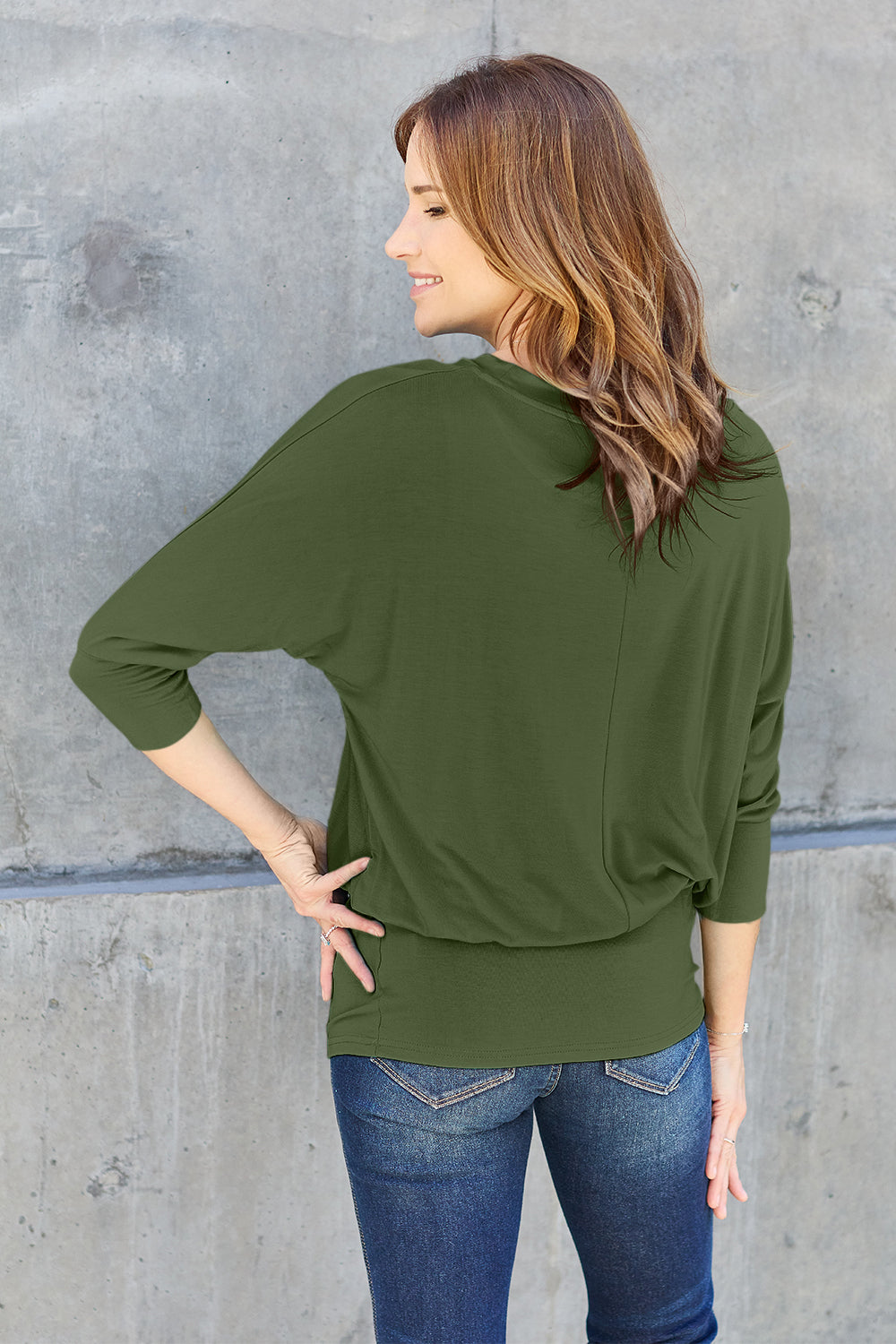 Woman wearing a green round neck batwing sleeve top, showcasing its basic style and slightly stretchy opaque fabric.