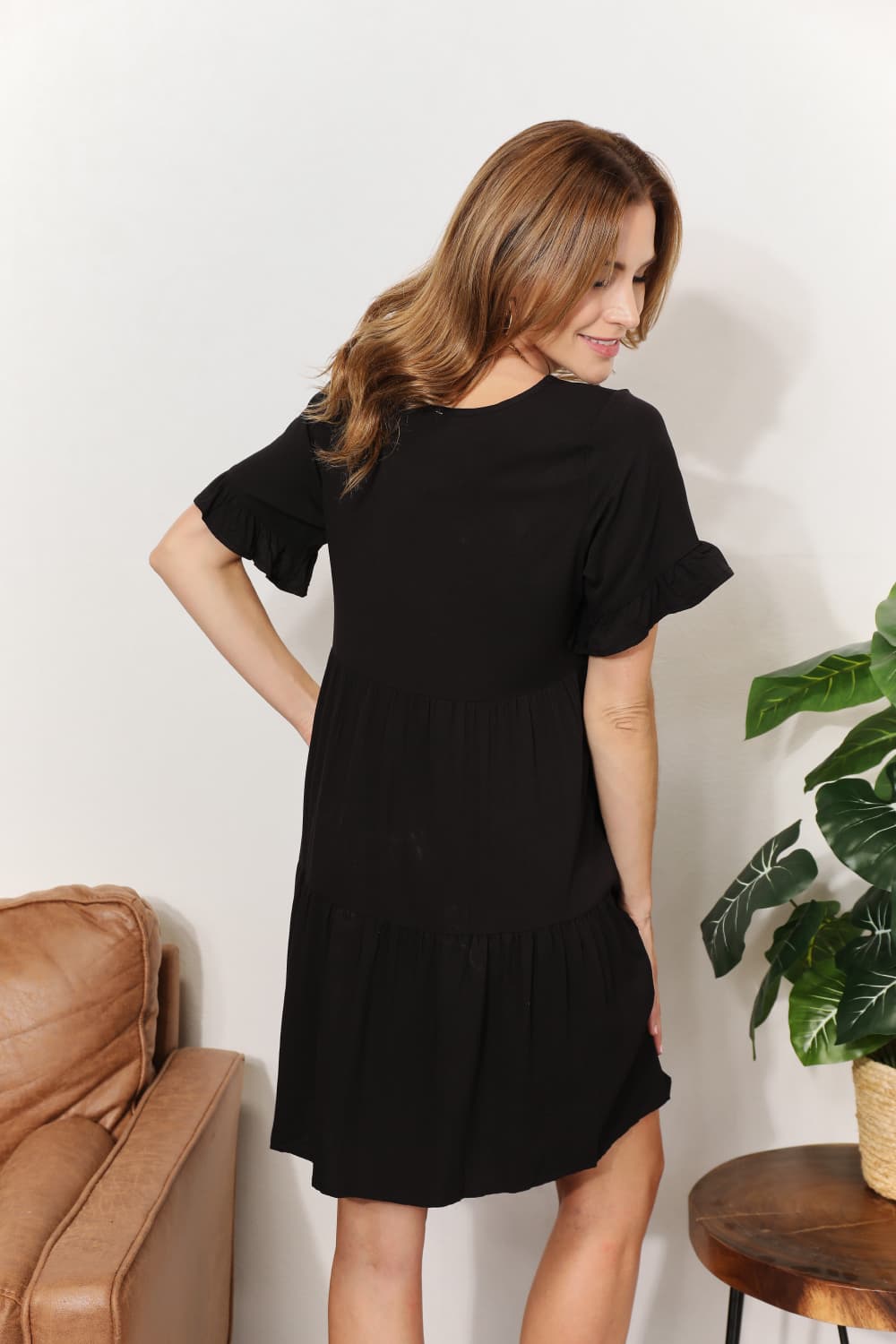 Woman wearing a black V-neck flounce sleeve tiered dress standing near a plant