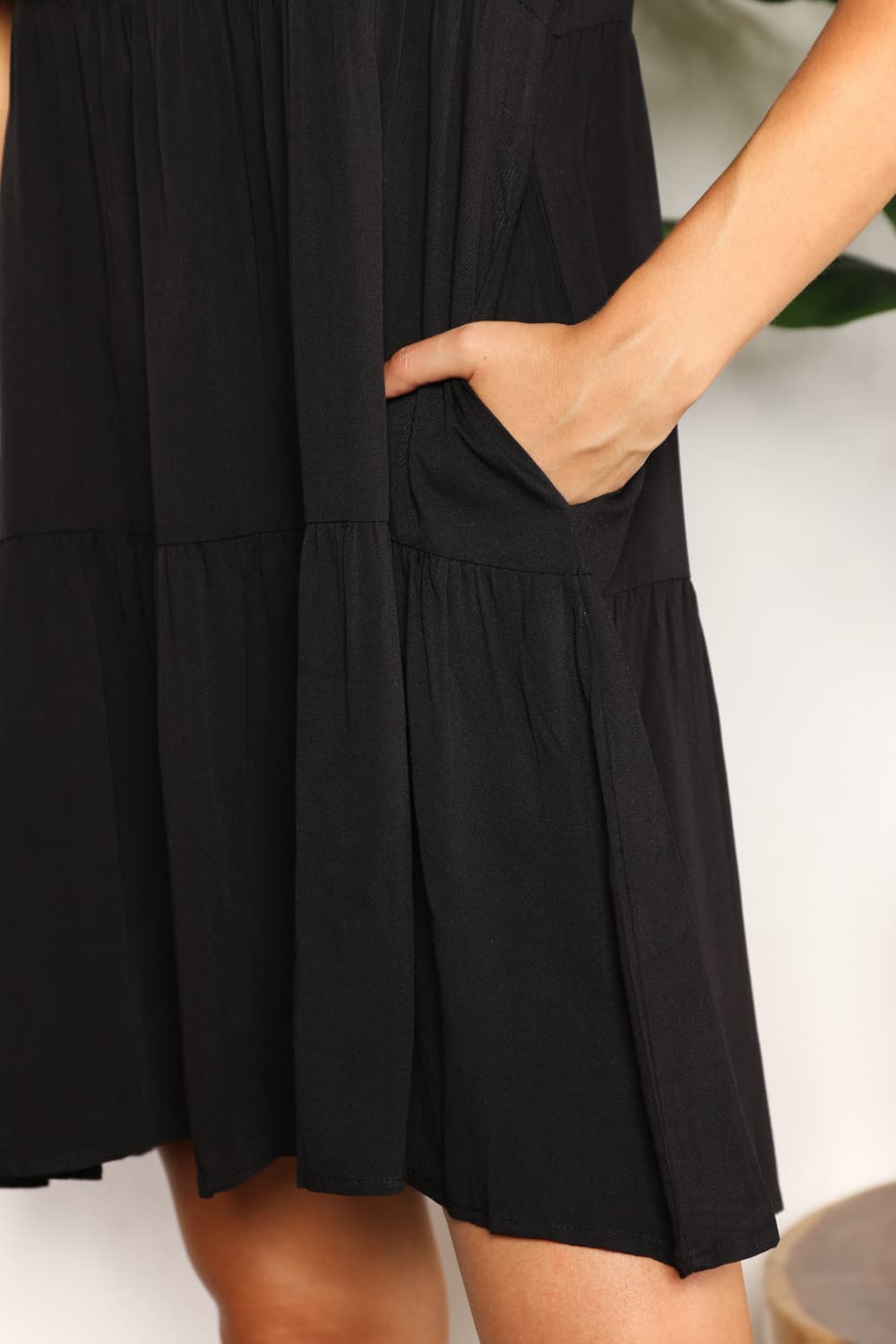 Black tiered dress with V-neckline and flounce sleeves, showcasing a chic knee-length design and convenient side pocket.