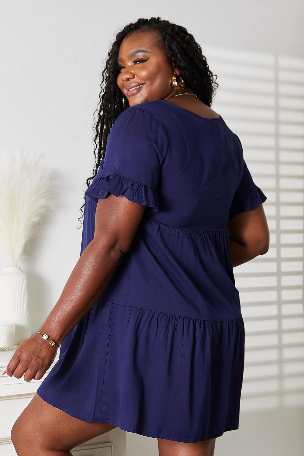 Woman wearing a navy V-neck flounce sleeve tiered dress with a smiling pose