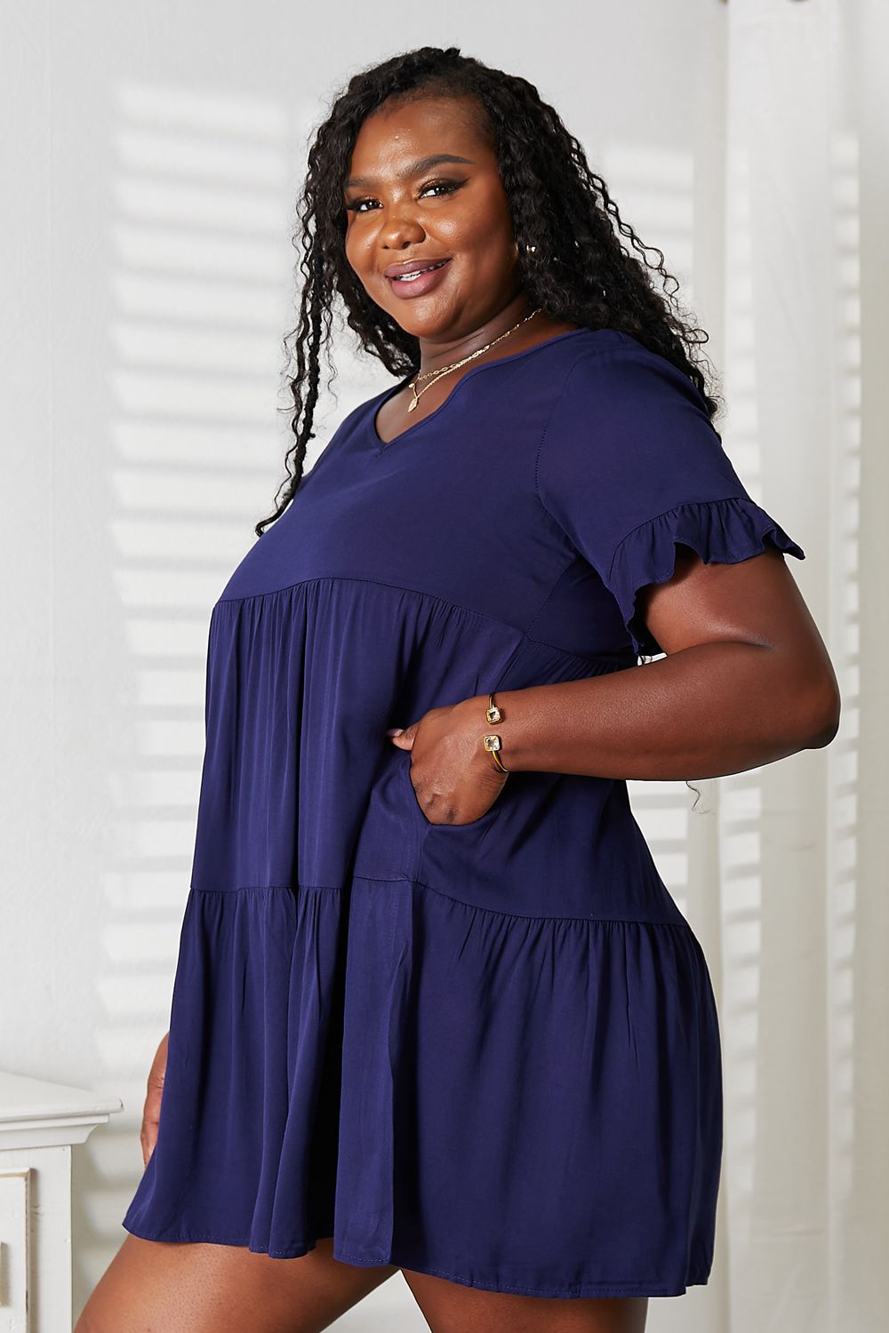 Woman wearing a navy V-neck flounce sleeve tiered dress with a confident smile.