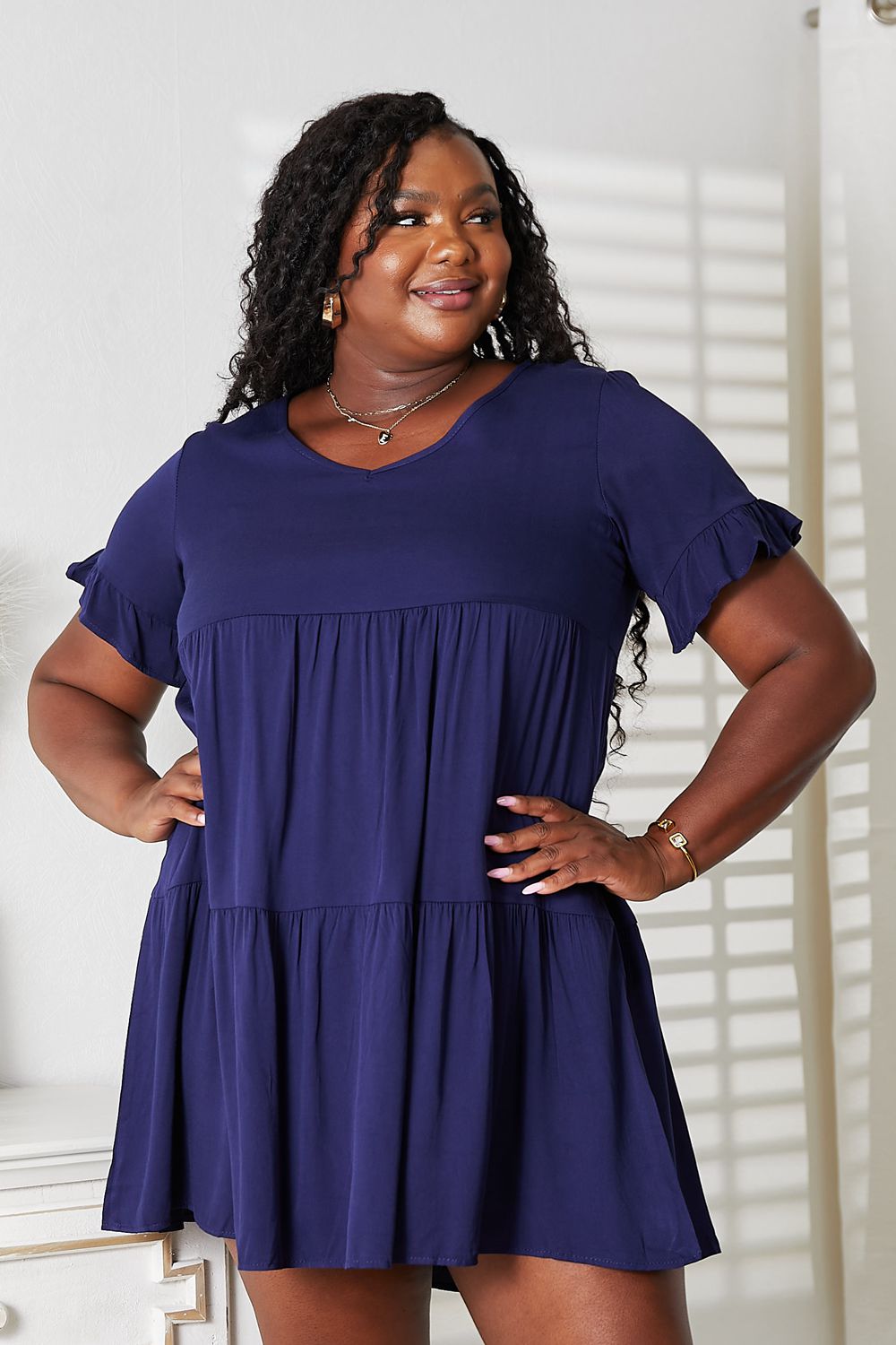 Woman wearing a navy blue V-neck flounce sleeve tiered dress with an elegant and feminine A-line design and playful flair.