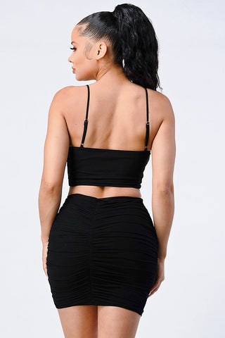 Woman wearing black Evelyn Mesh Cropped Cami and Skirt Set, showing back view with spaghetti straps and ruched skirt.