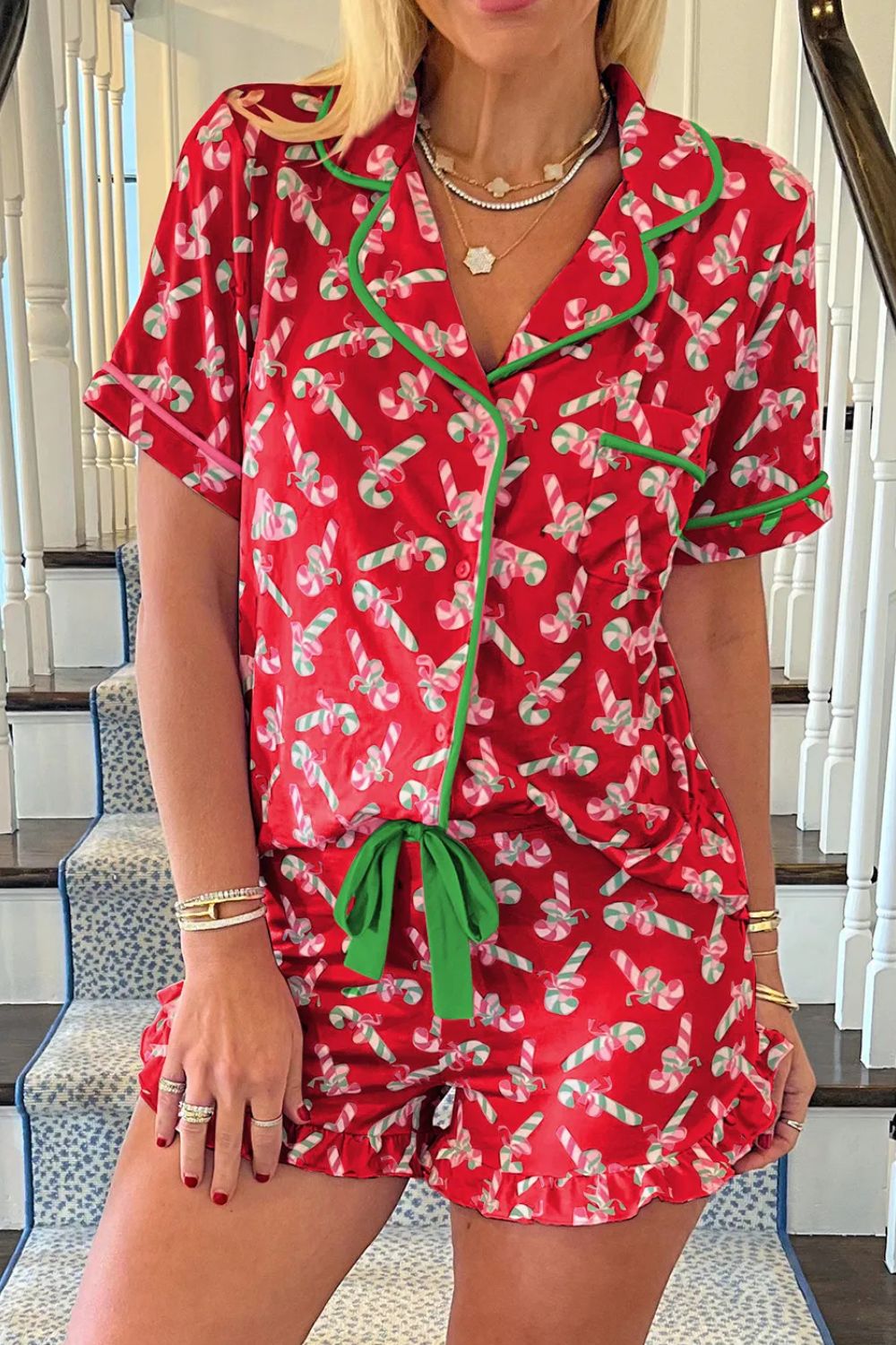 Woman wearing red candy cane collared neck top and shorts pajama set with green trim, standing on staircase.