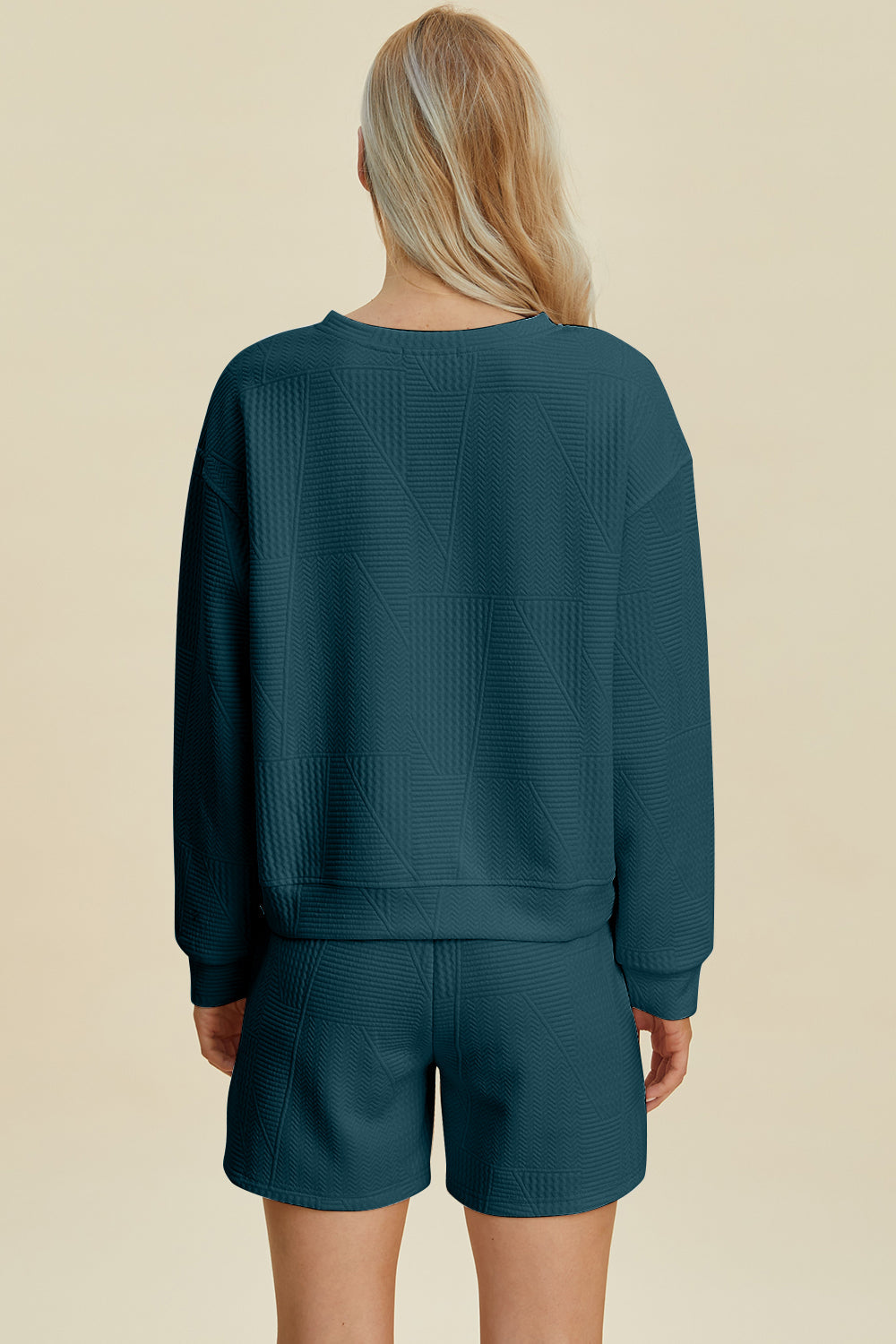 Woman wearing a teal long sleeve top and shorts set with textured pattern and round neck, made of polyester and elastane.