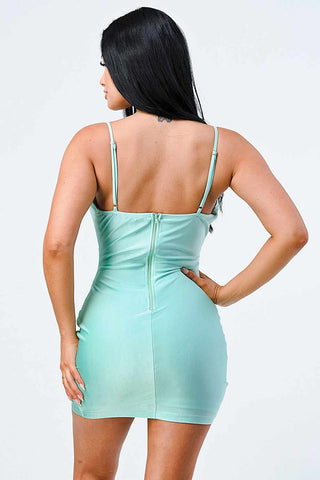 Woman in mint satin bodycon mini dress with cowl neck and adjustable straps, showcasing back view against neutral background.