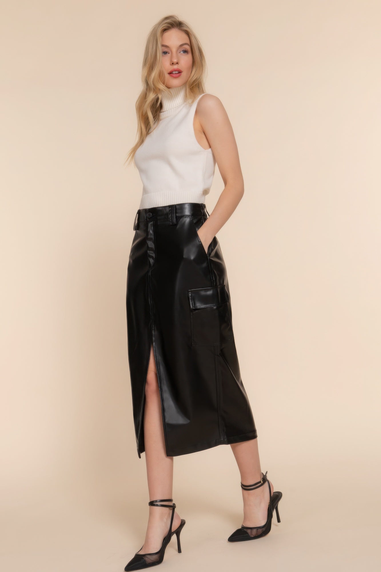 Woman wearing a sleek black faux leather midi cargo skirt with a side slit, paired with a sleeveless top and heels.