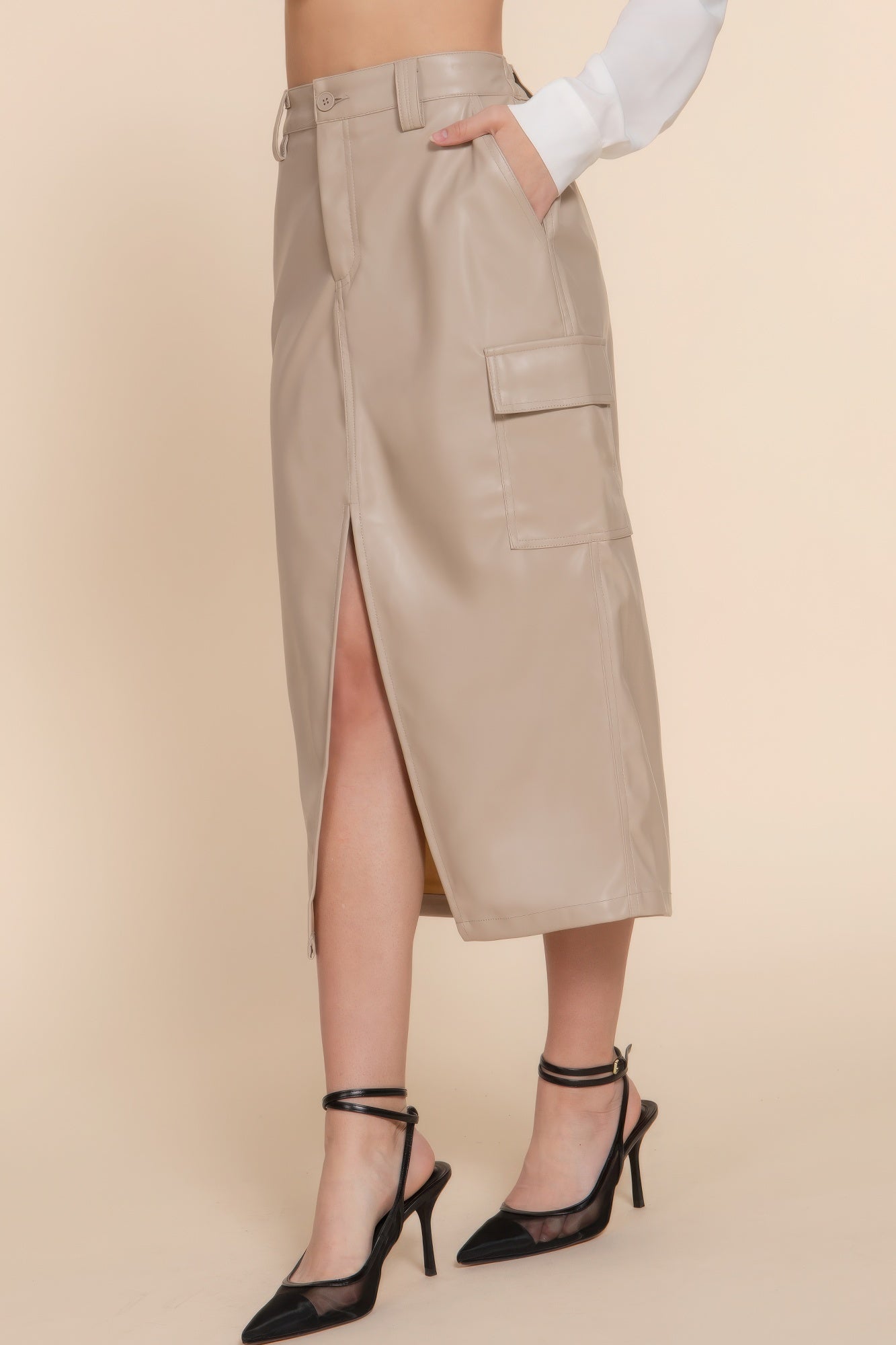 Faux leather midi cargo skirt in beige with side slit and pocket, paired with black heels for a stylish and edgy look.